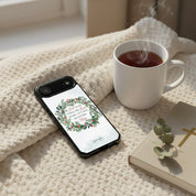 Cozy Christmas morning scene with a "Joy to the World" MagSafe iPhone case featuring a watercolor wreath, resting on a knit blanket next to a steaming mug of tea and a Bible.