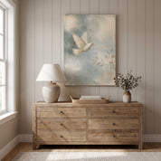 Led by the Spirit Christian dove canvas wall art above a rustic wooden dresser with a lamp, books and leafy vase against a neutral paneled wall.