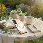 Love Never Ends Christian Samsung Galaxy phone case with 1 Corinthians 13:8 on a cafe table with an open Bible, a journal, a cup of tea, and succulents in a peaceful outdoor garden setting.