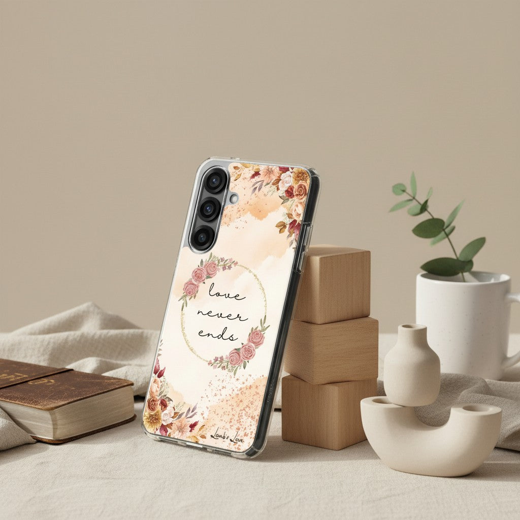 Love Never Ends Christian Samsung Galaxy phone case with a pink floral wreath and 1 Corinthians 13:8 verse, displayed in a lifestyle studio setting with a book and modern ceramic decor.