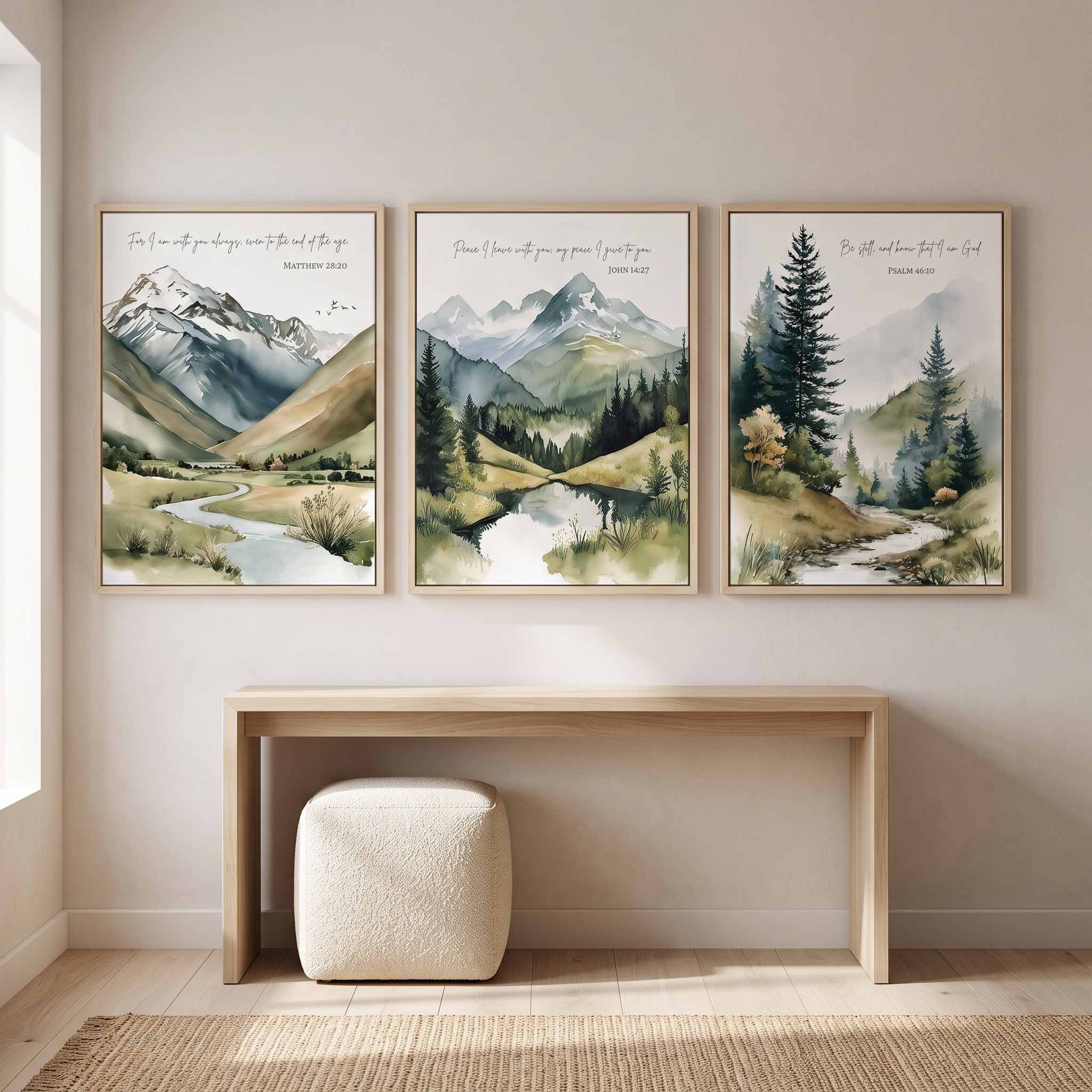 Three framed Christian mountain landscape wall art prints featuring Matthew 28:20, John 14:27, and Psalm 46:10 Scripture verses, displayed as a 3-piece triptych above a light wood console table in a bright modern entryway.