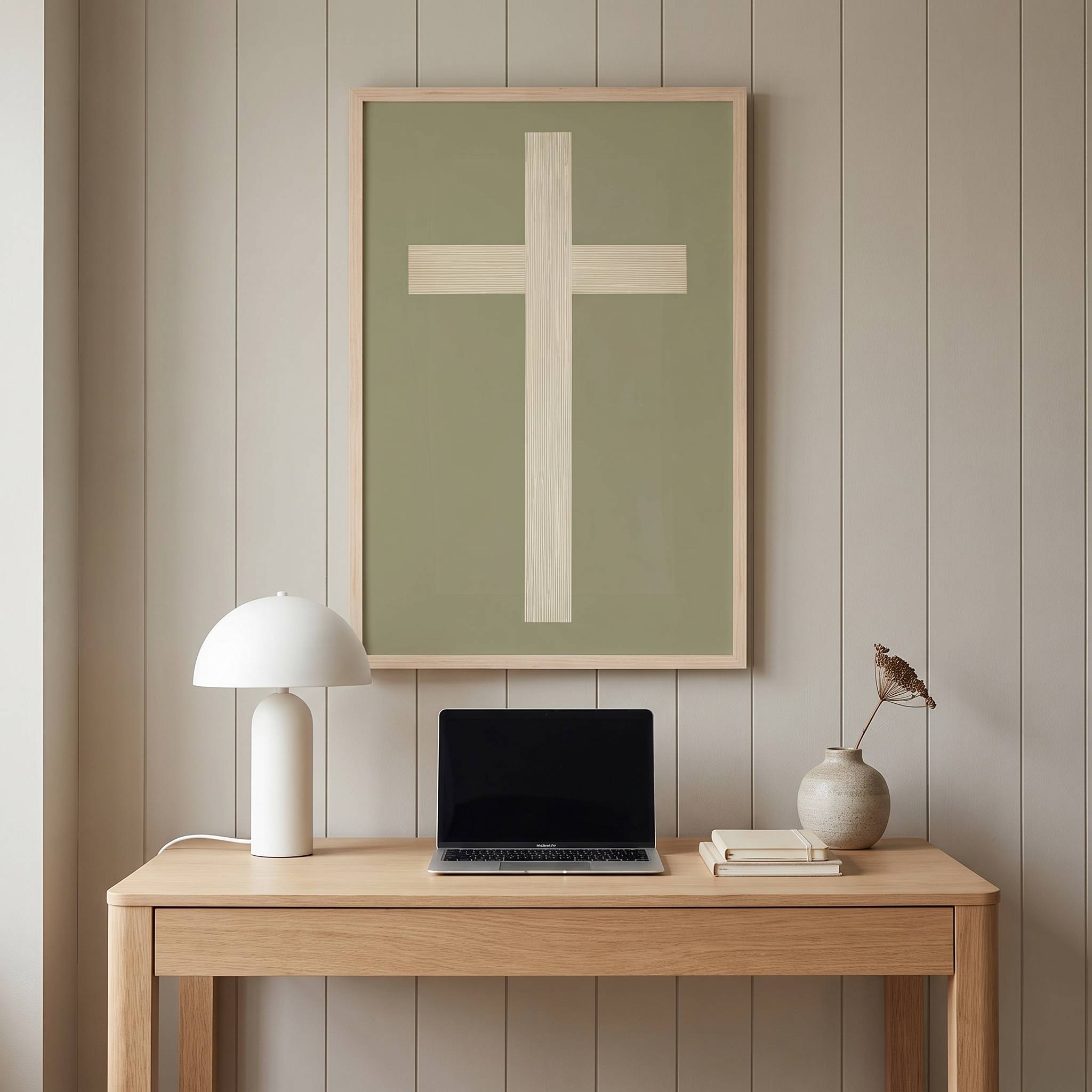Minimalist ivory cross vertical framed canvas wall art on a sage green background displayed above a light wood desk in an organic modern workspace.