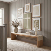 Minimalist ivory cross framed canvas centerpiece featured in a gallery wall with olive branch art above a light wood bench in an organic modern staircase entryway.
