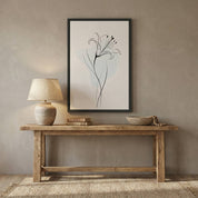 Minimalist Lily Line Art in a black frame, styled on a wooden console table with a ceramic lamp, books, and beads against a beige textured wall.