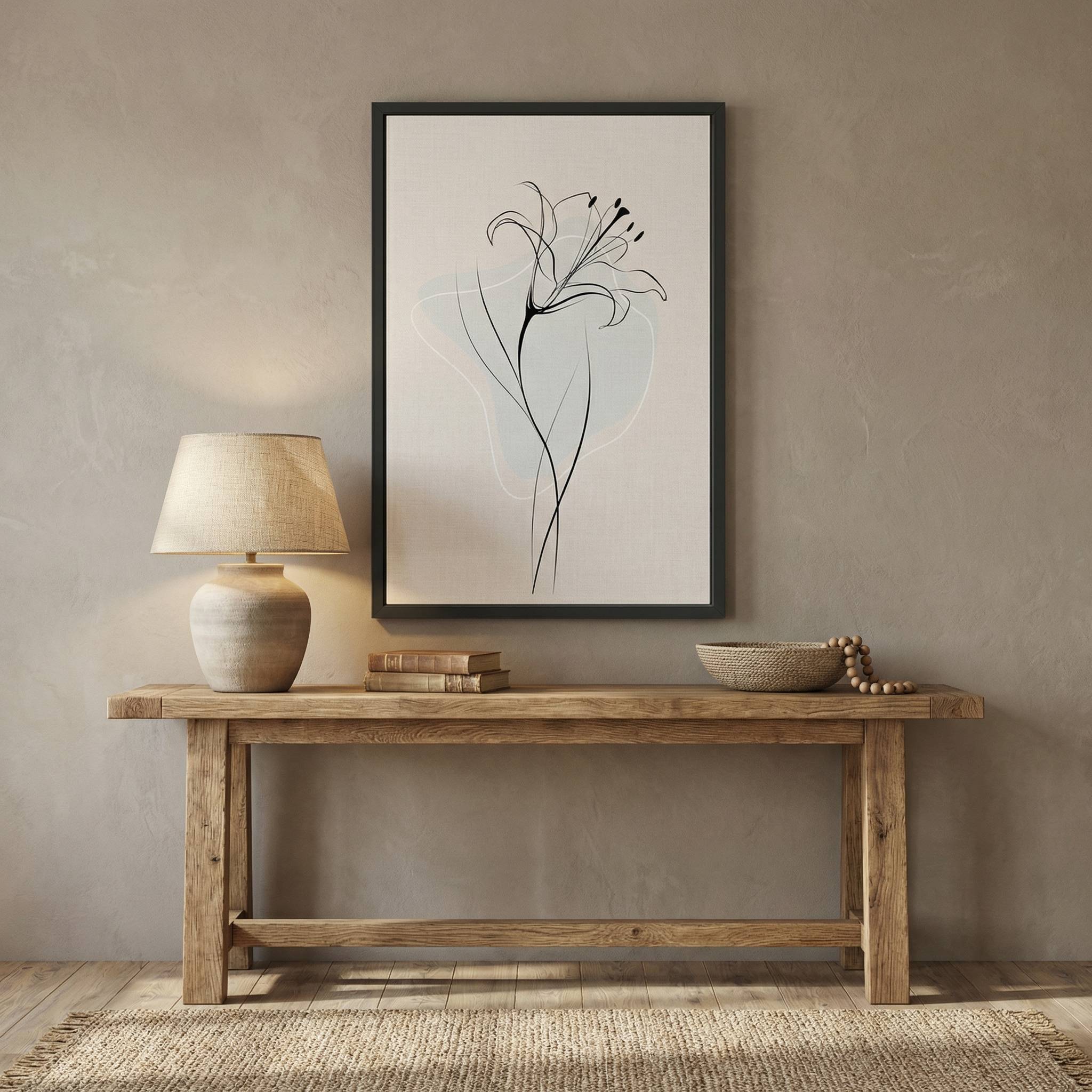 Minimalist Lily Line Art in a black frame, styled on a wooden console table with a ceramic lamp, books, and beads against a beige textured wall.