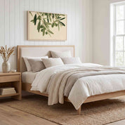 Minimalist olive branch horizontal framed canvas artwork displayed above a light wood bed in a soft organic modern bedroom.