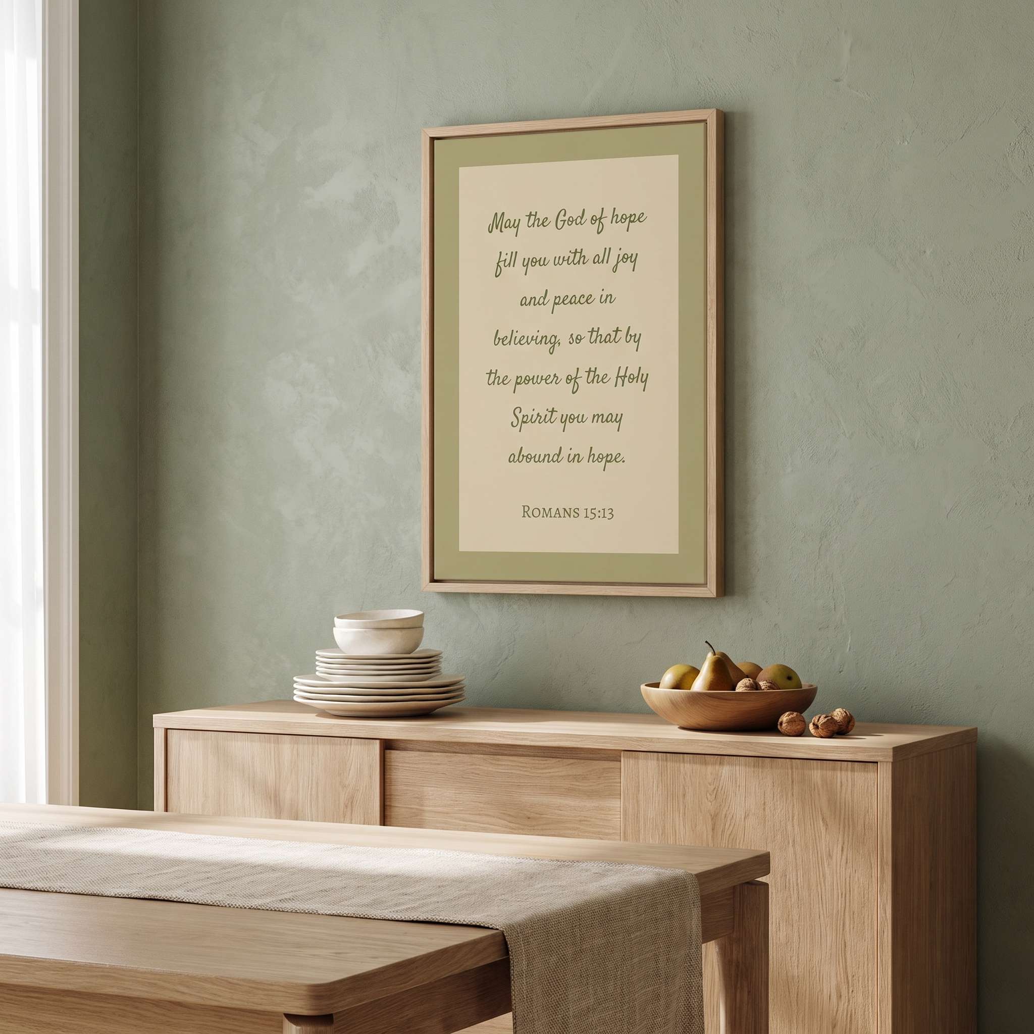 Minimalist Romans 15:13 Scripture vertical framed canvas wall art in soft sage green displayed on a textured plaster wall above a light wood sideboard in an organic modern dining room.
