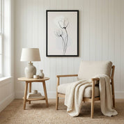 Framed minimalist tulip line art hanging in a cozy reading nook with a beige armchair, wooden side table, and cream textured throw blanket.