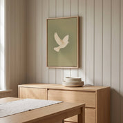 Minimalist white dove holy spirit vertical framed canvas wall art displayed on a beige paneled wall above a light wood sideboard in an organic modern dining room.