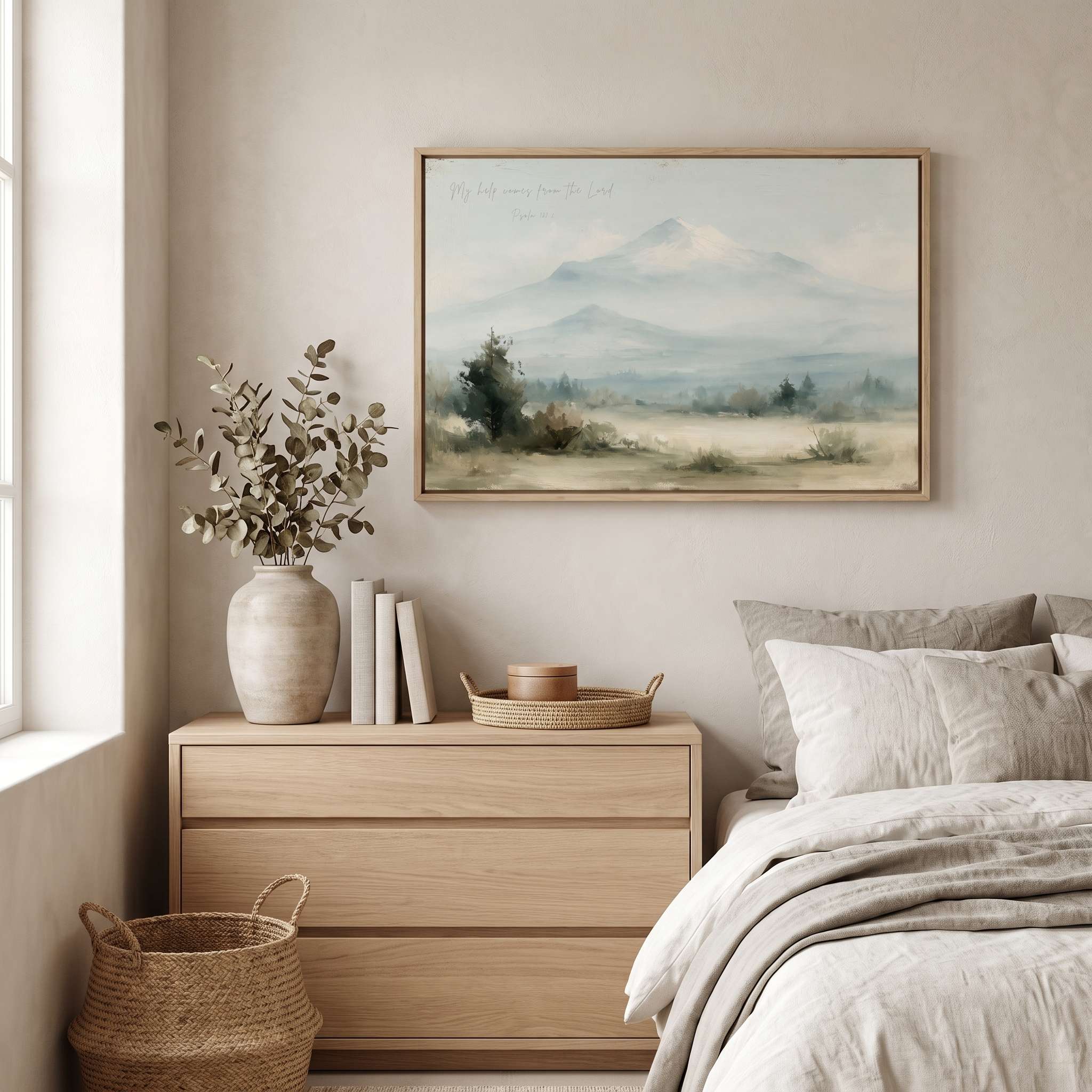 Framed vintage Psalm 121:2 Christian landscape canvas wall art featuring snow-capped mountains hanging on a beige wall above a light wood dresser nightstand and neutral linen bed in a soft organic modern bedroom.
