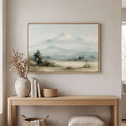 Framed vintage Psalm 121:2 Christian landscape canvas wall art featuring snow-capped mountains hanging above a light wooden console table with stacked books, a ceramic vase with dried flowers, and a woven basket in a beige entryway.