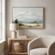 Framed vintage Psalm 121:2 Christian landscape canvas wall art featuring snow-capped mountains hanging above a light wooden console table with a ceramic table lamp and a textured beige armchair.