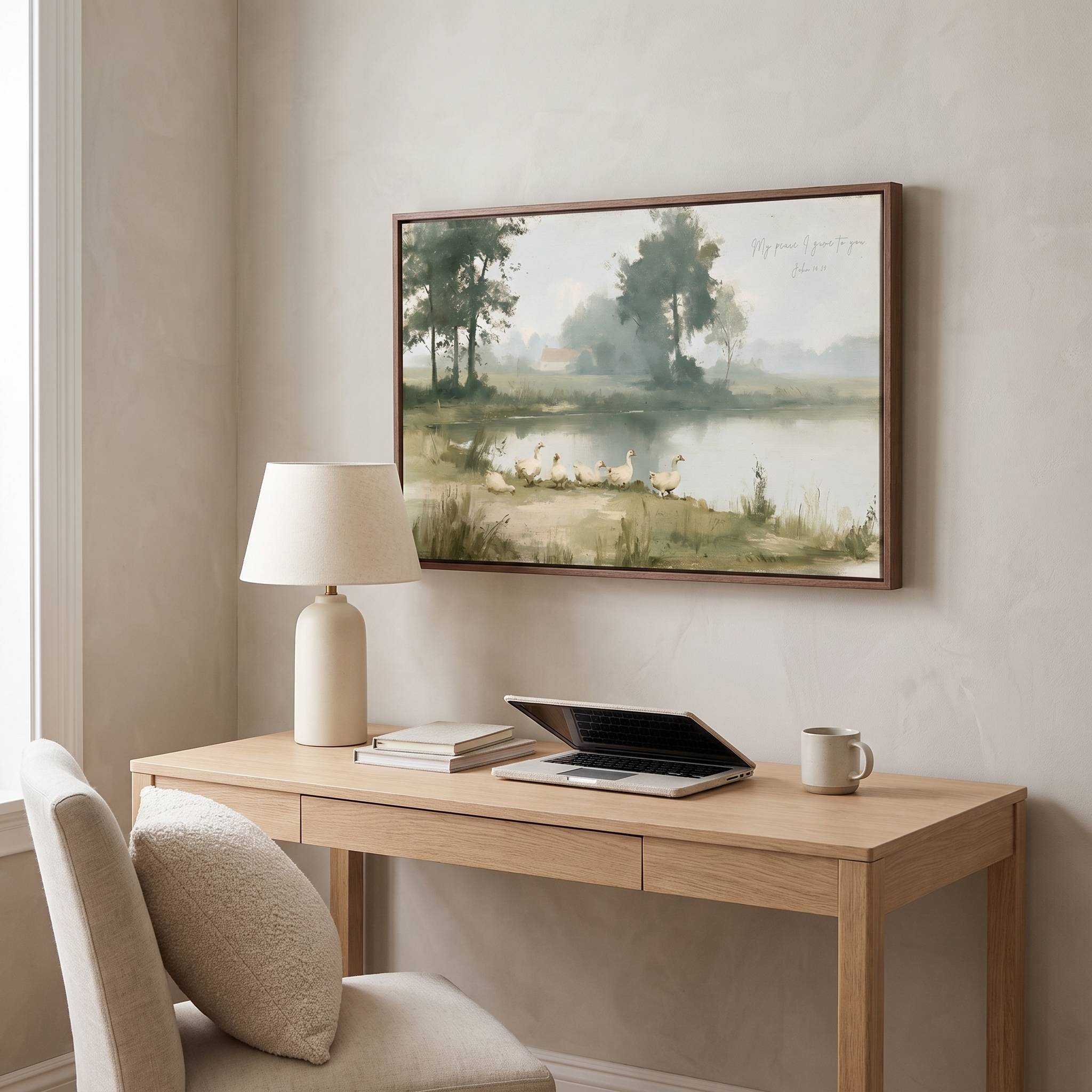 Framed vintage John 14:27 landscape canvas wall art hanging above a light wood desk with a lamp and laptop in a warm modern workspace.