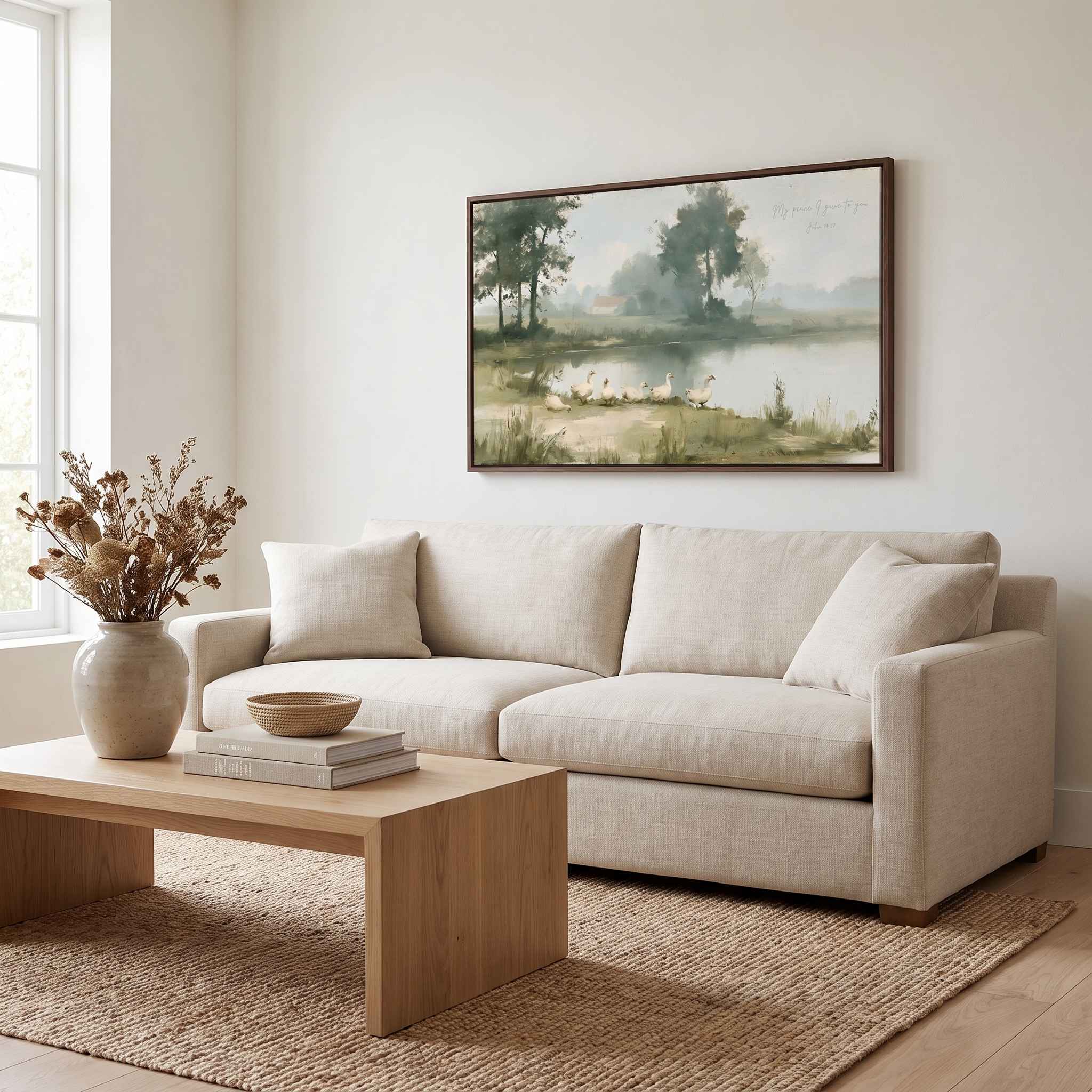 Framed vintage John 14:27 landscape canvas wall art hanging above a cream sofa and wooden coffee table in a bright modern living room.