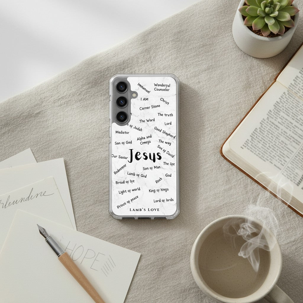 A clear Samsung Galaxy phone case with black typography of the Names of Jesus, placed on a beige textured surface next to an open book, a steaming white coffee mug, a small succulent, and a pen.