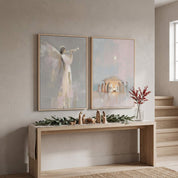 Christian Christmas wall art diptych with a Nativity scene and angel print above a console decorated with a wooden manger display and greenery.