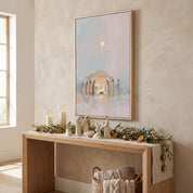 Framed watercolor Nativity wall art above an entryway console decorated with candles and greenery, a welcoming Christian Christmas display.