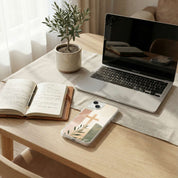 Laptop, notebook, and phone on a wooden table with a plant in the background