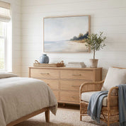 Framed vintage Mark 4:39 Christian landscape canvas wall art featuring a coastal beach scene hanging above a light wooden dresser with a rattan armchair in a cozy bedroom.