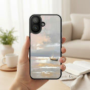 Peace Be Still MagSafe® clear iPhone case featuring a peaceful boat on calm ocean waters, held in hand beside an open book and coffee mug in a warm coastal-inspired home setting