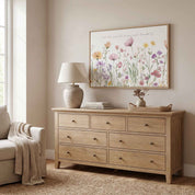 Framed Proverbs 3:5 wildflower wall art above a natural wood dresser with a lamp and books in a bright neutral room.