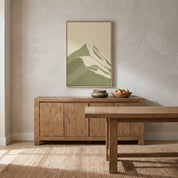 Framed minimalist mountain Scripture wall art titled Psalm 121:1–2 featuring layered sage green mountain peaks, displayed in a light wood frame on a warm textured beige wall above a rustic wooden sideboard and dining table in a modern organic dining room.