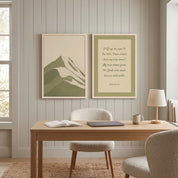 Two-piece framed canvas gallery wall set featuring Psalm 121:1–2 Scripture art and a minimalist sage green mountain landscape print, displayed in light wood frames on a warm beige vertical-paneled wall above a natural wood desk and cream bouclé chair in a bright modern home office.