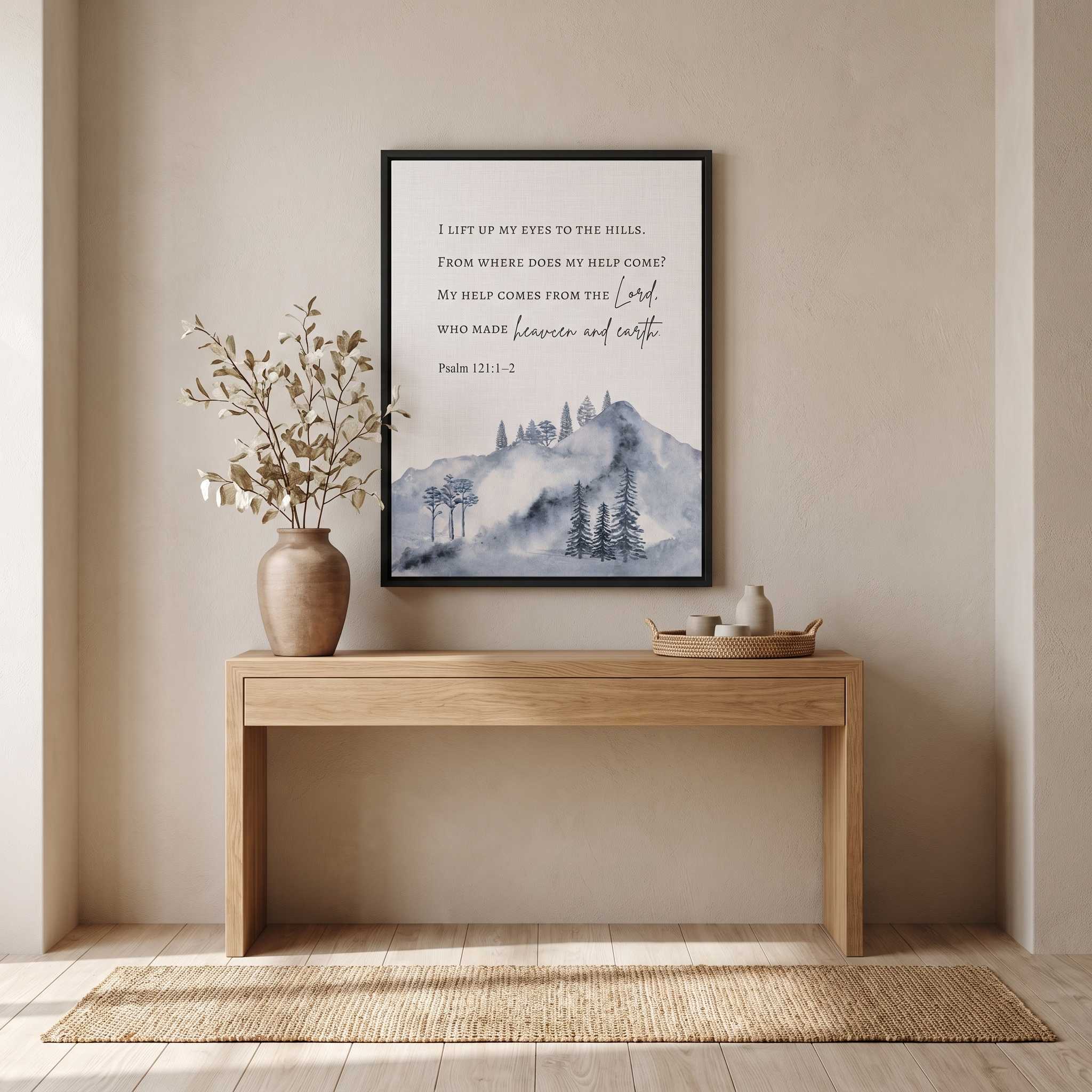 Framed Psalm 121:1–2 mountain Scripture wall art in soft blue gray watercolor, displayed above an entryway console with a vase and woven rug.