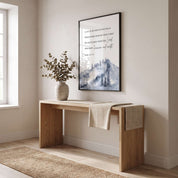 Framed Psalm 121 mountain Scripture wall art with a blue gray watercolor landscape, displayed above a light wood console with dried branches in a bright hallway.