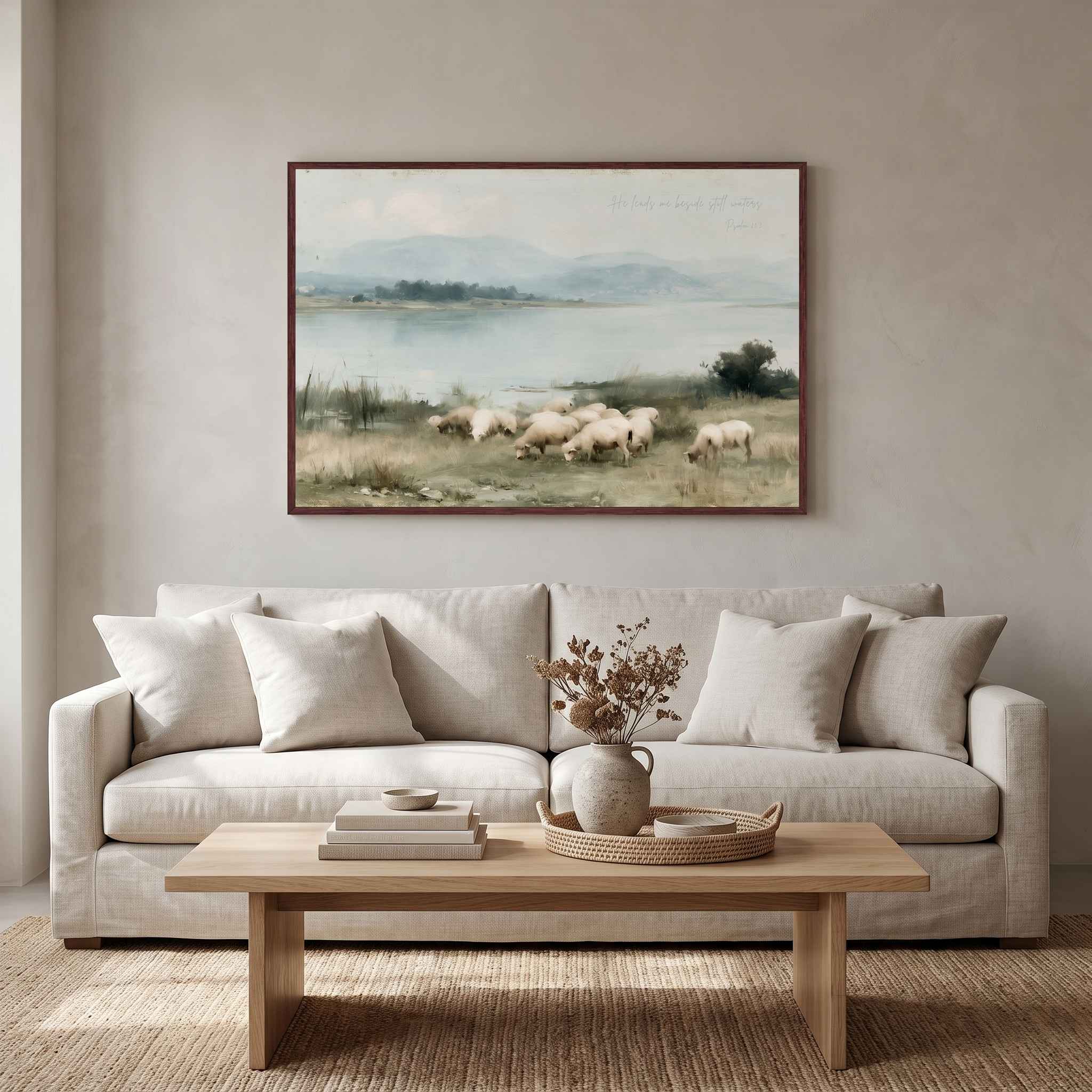 Framed Psalm 23 vintage landscape canvas art displayed above a beige sofa in a modern organic living room, featuring sheep grazing beside calm waters.