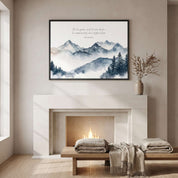 Psalm 33:9 mountain Scripture wall art with misty blue gray peaks and cursive Bible verse, framed above a fireplace with cozy blankets and a vase.
