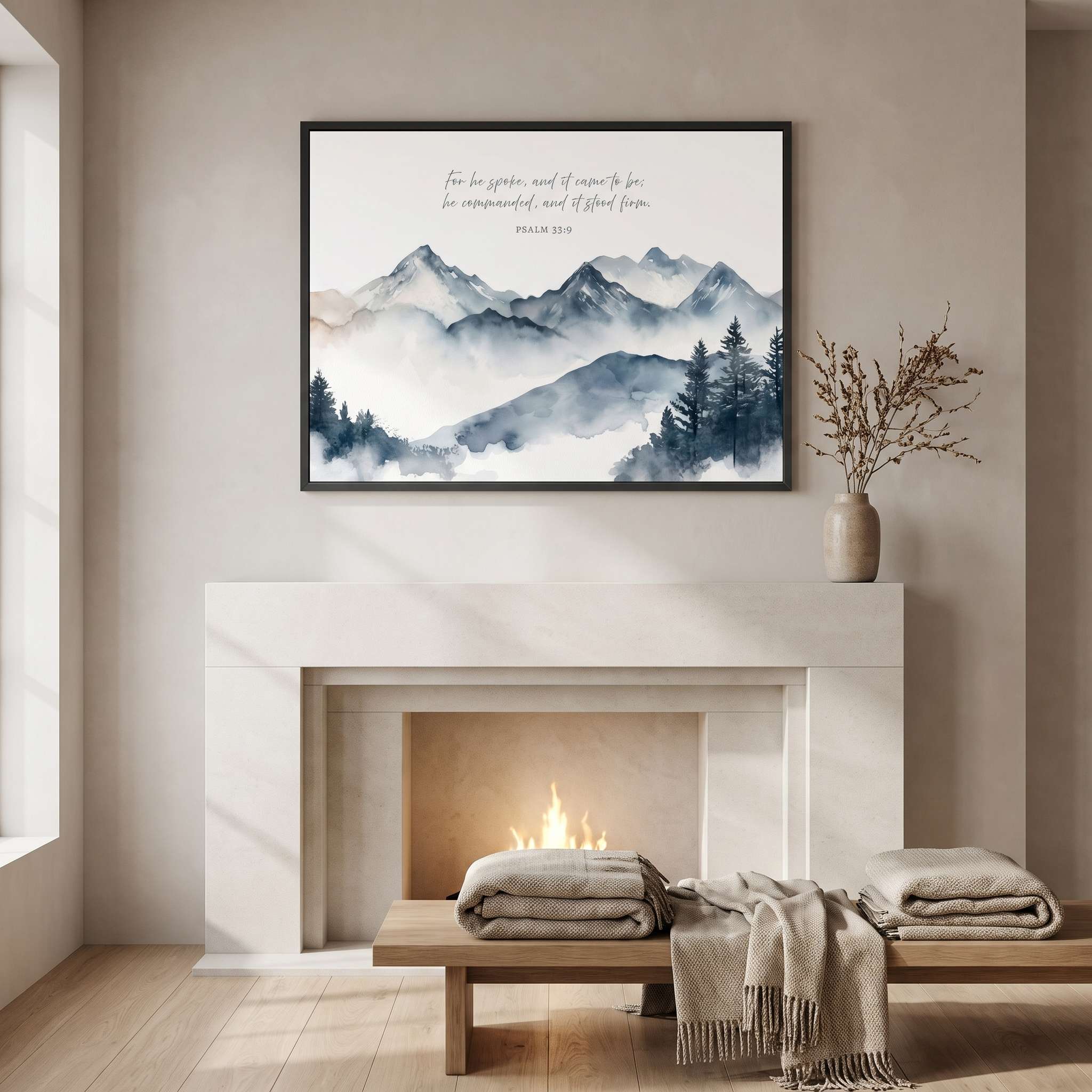 Psalm 33:9 mountain Scripture wall art with misty blue gray peaks and cursive Bible verse, framed above a fireplace with cozy blankets and a vase.