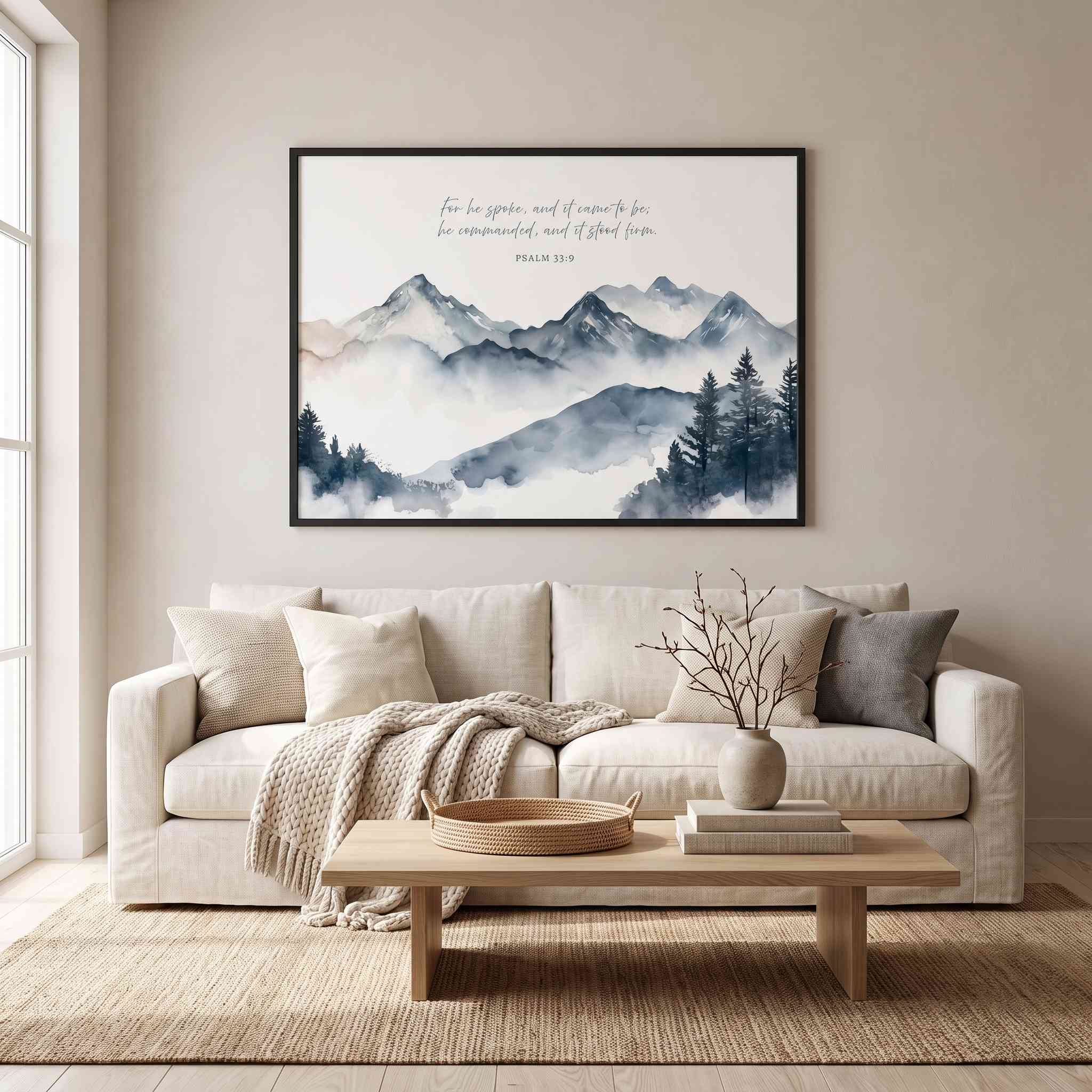 Psalm 33:9 mountain Scripture wall art with a misty watercolor landscape and cursive Bible verse, framed above a beige sofa in a bright living room.