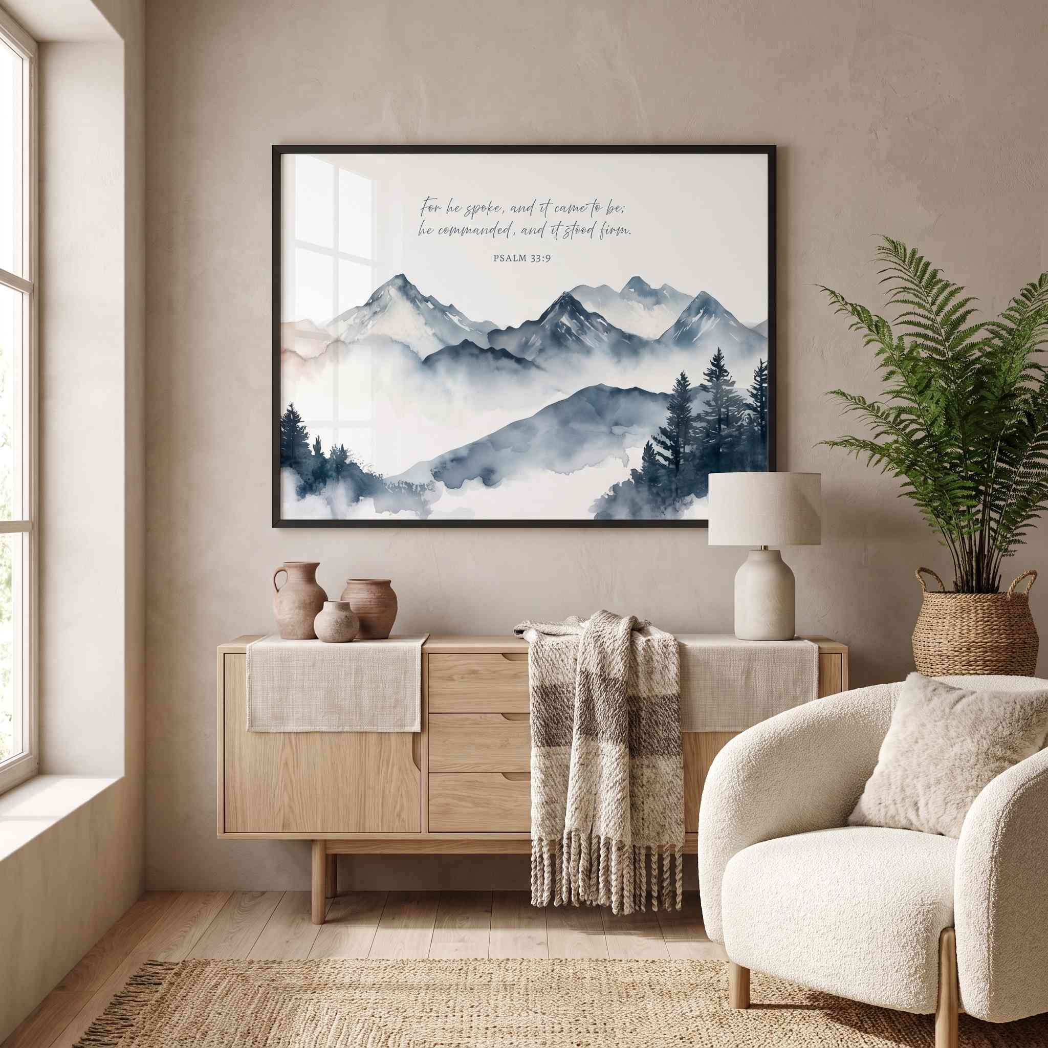 Framed Psalm 33:9 mountain Scripture wall art with misty blue gray peaks and cursive verse, styled above a light wood sideboard in a living room.