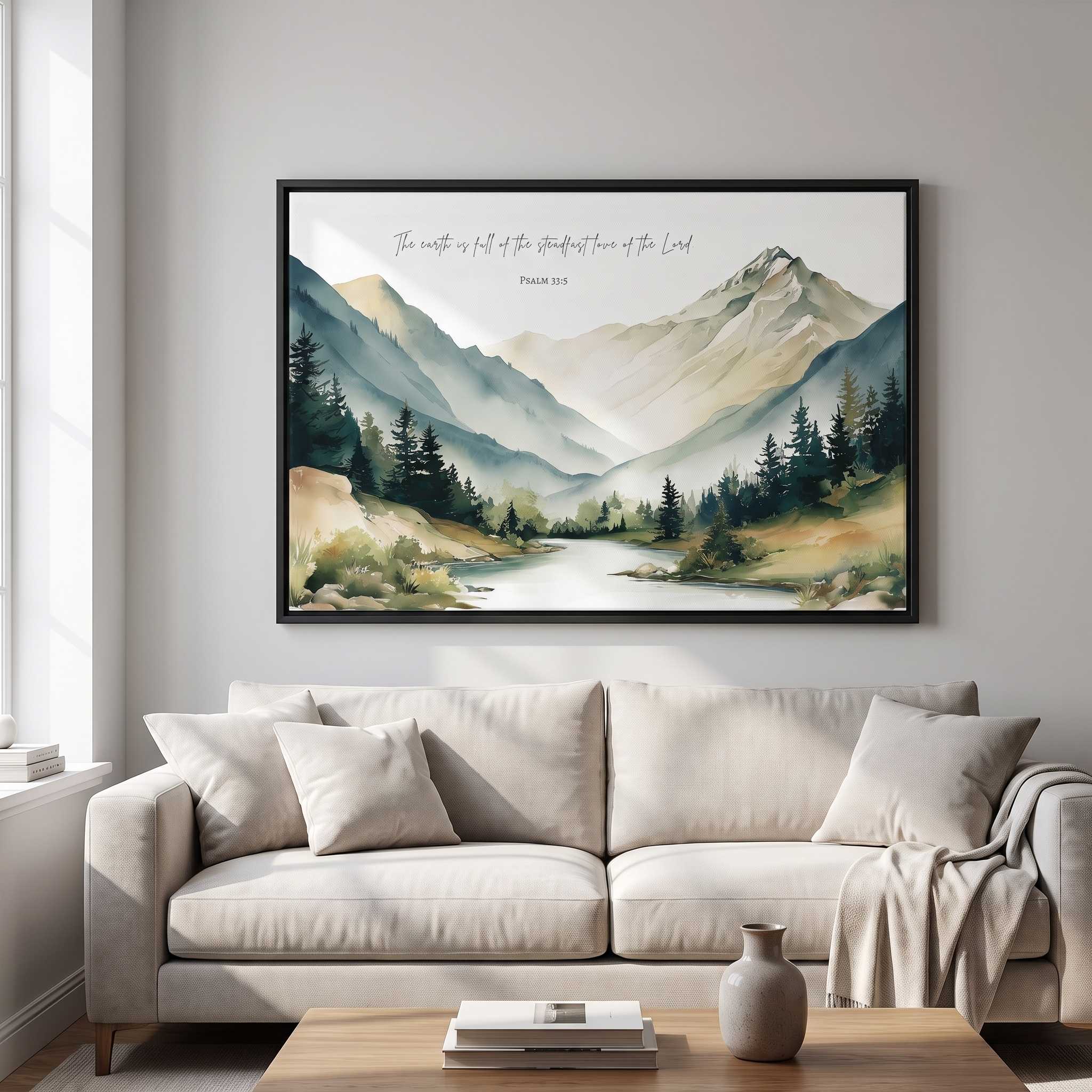 Framed vintage Christian mountain landscape wall art titled Psalm 33:5 featuring mountains, pine trees, and a river, displayed above a beige sofa in a modern minimalist living room.