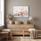 Psalm 34:8 pink wild rose Scripture wall art above a light wood bedroom dresser, with a lamp, books and woven benches in a warm neutral room.