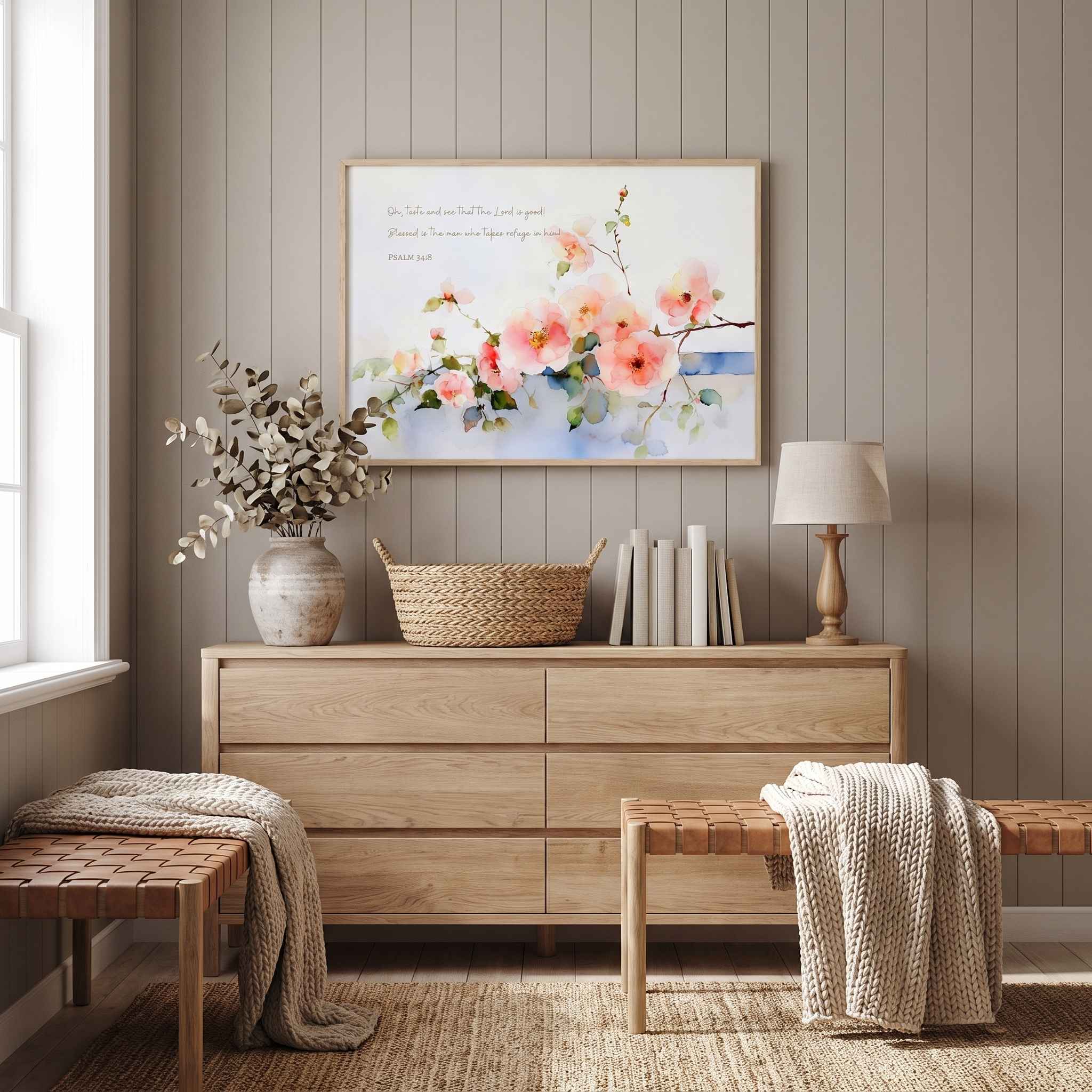 Psalm 34:8 pink wild rose Scripture wall art above a light wood bedroom dresser, with a lamp, books and woven benches in a warm neutral room.