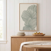 Framed minimalist palm leaf Scripture wall art titled Psalm 92:12–15 featuring "Flourish in Faith" with green line art artwork, displayed in a light wood frame on a white paneled wall above a wooden sideboard with decorative bowls in a soft organic modern dining room.