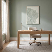 Framed minimalist palm leaf Scripture wall art titled Psalm 92:12–15 featuring "Flourish in Faith" with green line art artwork, displayed in a light wood frame on a sage green wall above a light oak desk and bouclé chair in a bright modern home office.
