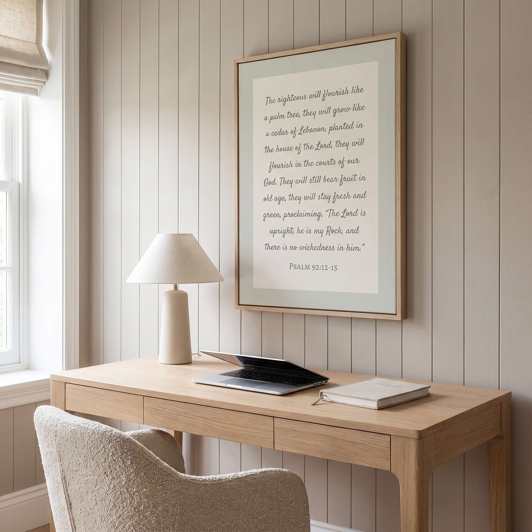 Framed minimalist Scripture wall art titled Psalm 92:12–15 featuring "The righteous will flourish like a palm tree" in elegant script, displayed in a light wood frame on a warm beige vertical-paneled wall above a natural wood desk with a ceramic lamp, laptop, and bouclé chair in a bright modern home office.