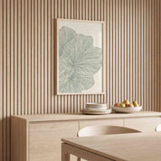 Framed minimalist palm leaf Scripture wall art titled Psalm 92:12–15 featuring "Flourish in Faith" with green line art artwork, displayed in a light wood frame on a slatted wood accent wall above a matching wood sideboard in a soft organic modern dining room.