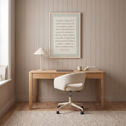 Framed minimalist Scripture wall art titled Psalm 92:12–15 featuring "The righteous will flourish like a palm tree" in elegant script, displayed in a light wood frame on a beige paneled wall above a natural wood desk with a ceramic lamp, laptop, and cream bouclé chair in a bright modern home office.