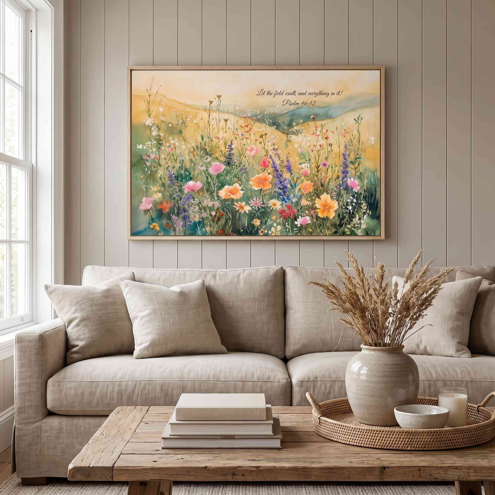 Psalm 96:12 wildflower meadow wall art above a beige sofa in a neutral living room, with colorful watercolor flowers and rolling hills.