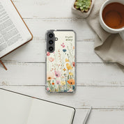 Rejoice Always Christian Samsung phone case with colorful wildflower design on a white painted wood surface next to an open Bible, a cup of coffee, and a small succulent.