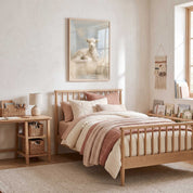 Rest by Still Waters Christian lamb framed print above a wooden bed with cream and dusty rose bedding, beside books and a desk in a child’s bedroom.