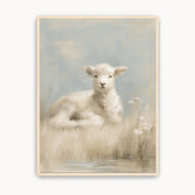 Rest by Still Waters Christian lamb wall art showing a white lamb resting beside quiet water and delicate wildflowers, in soft blue and cream tones with a light wood frame.
