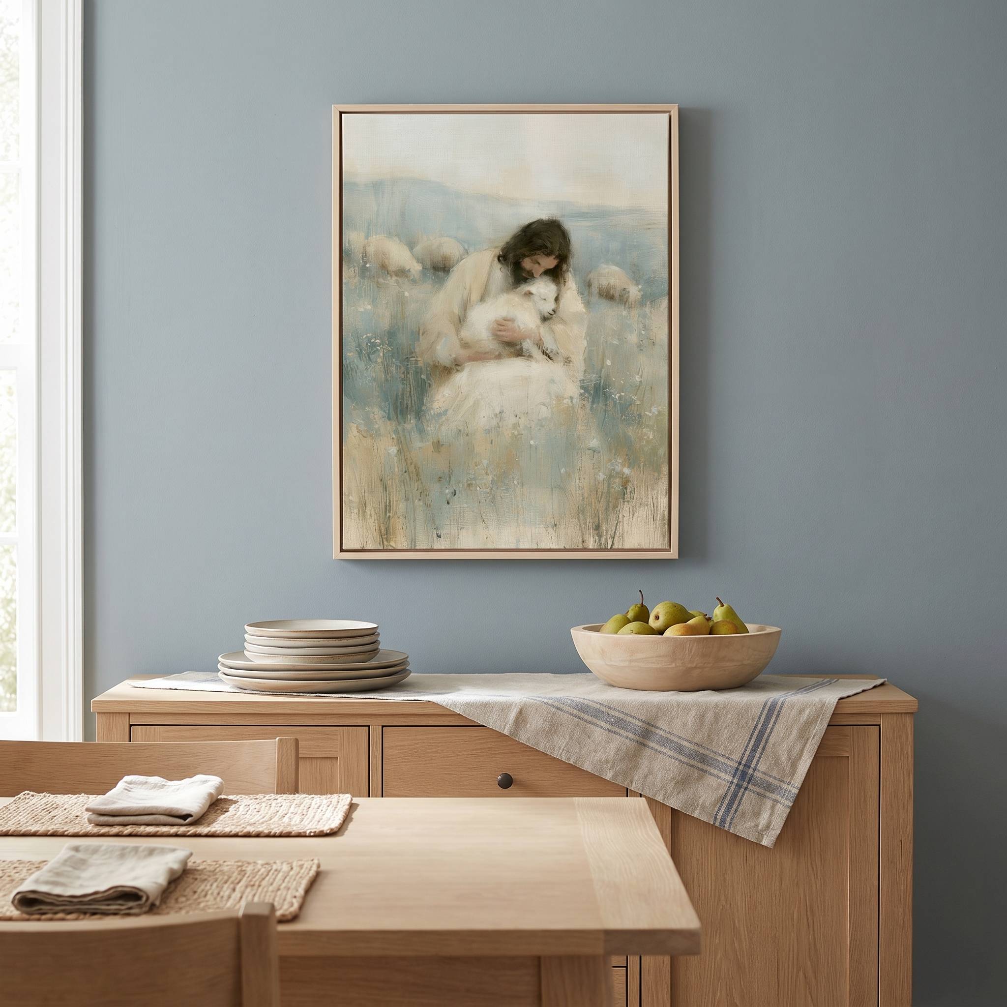 Framed Rest in His Arms Jesus holding a lamb Christian wall art on a blue-gray wall above a wooden dining room sideboard with plates and a fruit bowl.