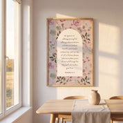 Framed vintage Christian floral wall art titled Romans 5:3–5 featuring "Hope does not put us to shame" with watercolor botanical artwork, displayed in a light wood frame on a beige wall above a wooden table in a sunlit Scandinavian dining room.