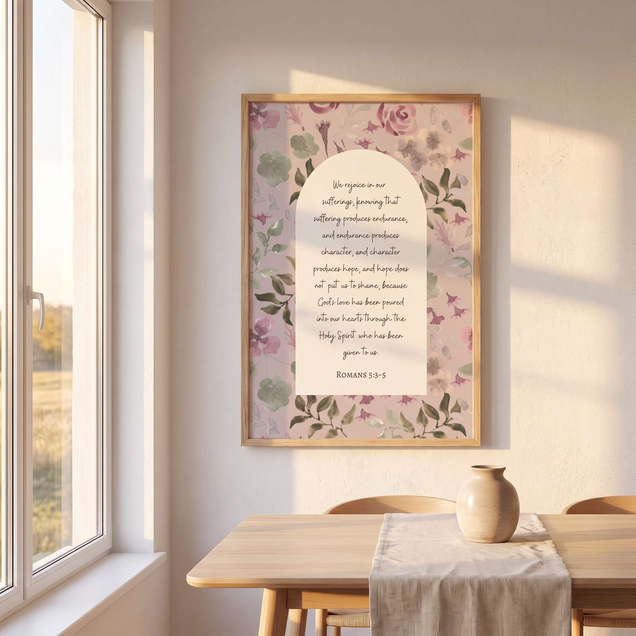 Framed vintage Christian floral wall art titled Romans 5:3–5 featuring "Hope does not put us to shame" with watercolor botanical artwork, displayed in a light wood frame on a beige wall above a wooden table in a sunlit Scandinavian dining room.