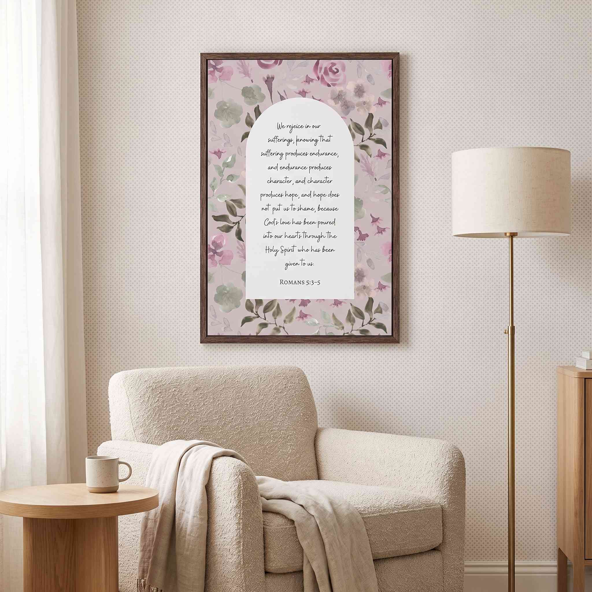 Framed vintage Christian floral wall art titled Romans 5:3–5 featuring "Hope does not put us to shame" with watercolor botanical artwork, displayed on a light wall above a beige armchair and floor lamp in a soft organic modern reading nook.
